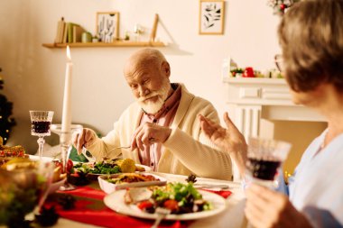 A senior couple shares laughter while savoring a festive Christmas meal at home filled with love. clipart