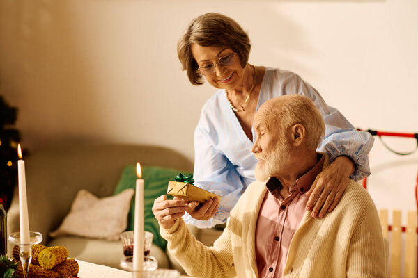 Любящая старшая пара делится сердечным моментом дома во время Рождества, обмениваясь подарками.