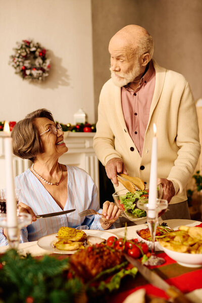 A senior couple shares a delightful Christmas meal, filled with smiles and love in their cozy home.