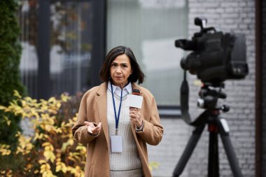 Çok ırklı bir kadın gazeteci mikrofona konuşuyor, dışarıda flaş haber yapmanın özünü yakalıyor..