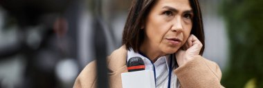 Çok ırklı bir kadın gazeteci, son dakika gelişmelerini aktarmaya hazırlanırken bir mikrofon tutuyor..