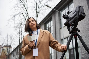 A woman journalist stands confidently with a microphone in hand, ready to deliver news outside. clipart