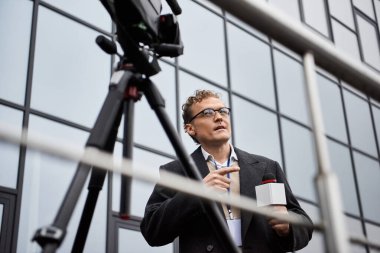 A professional journalist in glasses engages with a microphone, capturing news on location. clipart