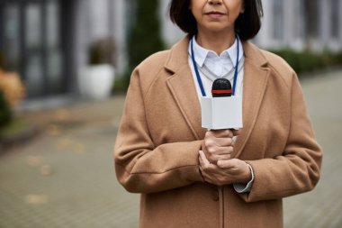 Kadın bir gazeteci mikrofon tutuyor, canlı bir şehir ortamında flaş haber vermeye hazırlanıyor..