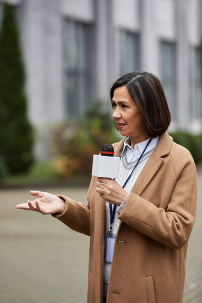 Многорасовая журналистка держит микрофон, освещая новости на открытом воздухе, демонстрируя свой профессионализм..