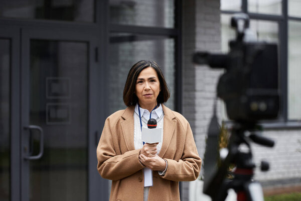 A journalist stands confidently outside, microphone in hand, ready to deliver important news coverage.
