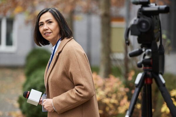 Мультирасовый журналист с микрофоном взаимодействует с аудиторией на улице, делясь важными новостями.