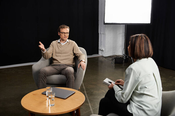 A journalist engages a specialist in a thoughtful discussion during a professional interview in a studio.