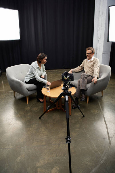 A skilled journalist engages in a thoughtful conversation with a subject expert in a contemporary studio.