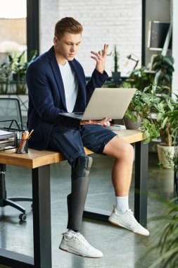 Yapay bacaklı genç bir girişimci masadayken dikkatle dizüstü bilgisayarına odaklanır..