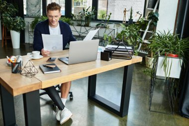 A determined young businessman with an artificial limb reviews documents at his desk in a stylish office. clipart