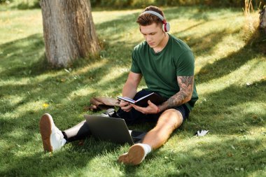 Protez bacaklı genç bir adam çimlerin üzerinde oturur, açık hava güneşinin tadını çıkarırken defterine odaklanır..