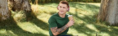 Genç bir adam dışarıda dinleniyor, kahve içiyor ve kulaklıkla müzik dinliyor..