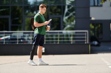 Protez bacaklı genç bir adam dışarıda duruyor, kahvesini yudumluyor ve güneş ışığında telefonuna odaklanıyor..
