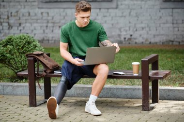 Protez bacaklı genç ve yakışıklı bir adam dışarıda bir bankta dinlenirken dizüstü bilgisayarıyla çalışıyor..