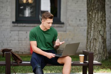 A young man with a prosthetic leg engages in work outdoors, surrounded by greenery and a coffee cup nearby. clipart