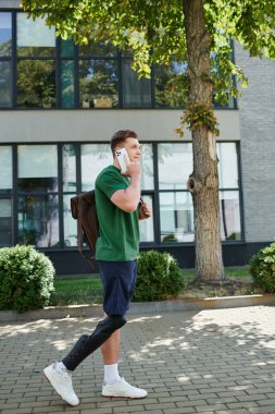 A young and handsome man with a prosthetic leg walks confidently while talking on his phone. clipart