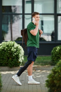 Protez bacaklı genç bir adam canlı bir açık hava sahnesinde telefonuyla sohbet ederken gülümsüyor..