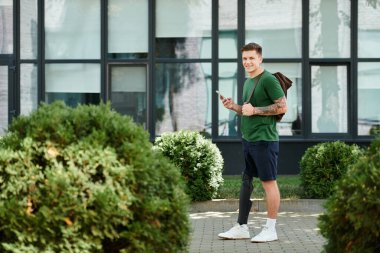 Protez bacaklı genç bir adam açık havada duruyor, telefonunu tutarken gülümsüyor..