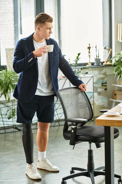 A young businessman with an artificial limb stands confidently, sipping coffee in a stylish office.