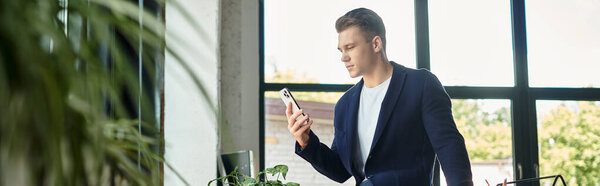 A young businessman focuses on his smartphone while working in a bright office.