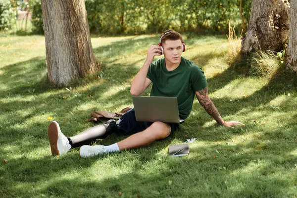 Protez bacaklı genç bir adam açık havada güneşli bir günün tadını çıkarırken yeşil çimlere oturur..