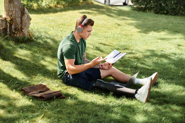 Молодой человек расслабляется на траве, читает книгу, занимаясь спортом на протезной ноге, наслаждаясь летним отдыхом.