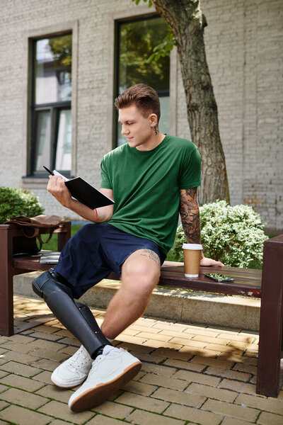 Молодой человек с протезной ногой сидит на скамейке и пишет в блокноте, наслаждаясь природой..