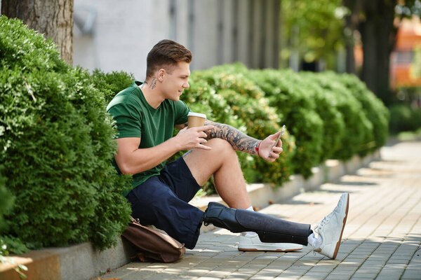 A young man with a prosthetic leg relaxes on a sunny day, sipping coffee and enjoying his surroundings.