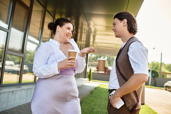 A young plus size woman engages in a lively chat with her friend over coffee in the sun.