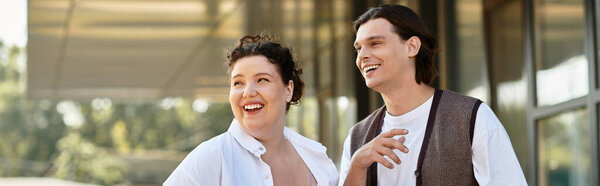 A cheerful young plus size woman laughs alongside her male friend in a sunny outdoor setting.
