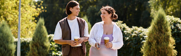 A young plus size woman and her male friend stroll in a sunny park, smiling with coffee.