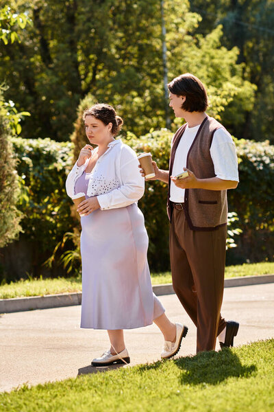 Two friends enjoy a leisurely walk in the park, sipping drinks and sharing laughter.