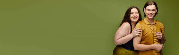 Веселая молодая женщина плюс размер обнимает свою подругу, обе ярко улыбаются на зеленом фоне.
