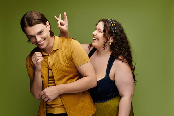 A cheerful young plus size woman has fun with her male friend while posing together, smiling.