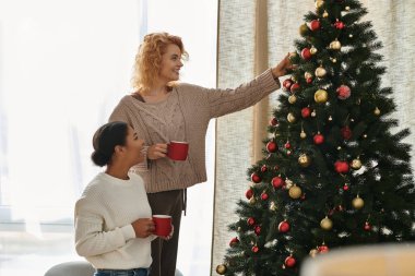 İki kadın, mutlu bir Noel ağacını evlerinde süslerken aynı kahkaha ve sevgiyi paylaşıyor..