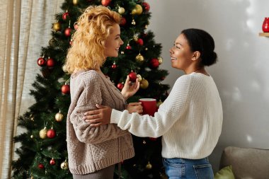 İki kadın evdeki süslü bir Noel ağacının önünde sıcak bir anı paylaşıyor..