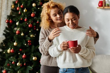 Bir çift, şenlikli bir yaşam alanında sıcak içeceklerin tadını çıkarırken birbirlerine sıcak bir şekilde gülümserler..