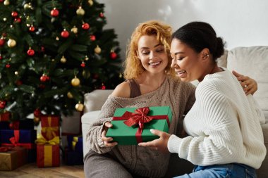 Two partners share a lovely moment exchanging a beautifully wrapped gift during the holidays. clipart