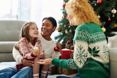 Neşeli bir lezbiyen çift Noel 'i kızlarıyla birlikte süslü bir ağacın yanında kutluyor..