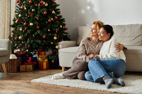 Две женщины тепло обнимаются на полу, наслаждаясь компанией друг друга во время праздников.