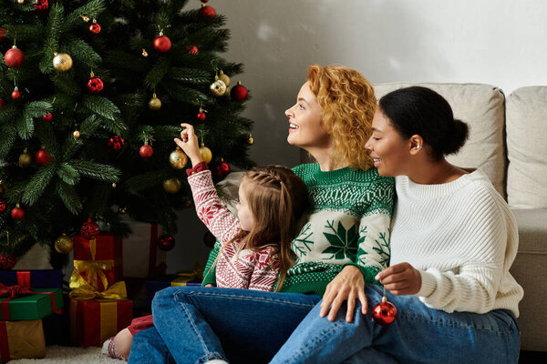 Любящая пара разделяет теплый момент, украшая праздничную елку со своей дочерью.