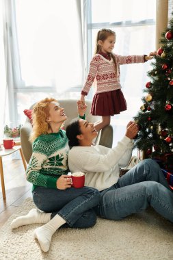Sevgi dolu bir çift, kızları Noel ağacını neşeyle süslerken kahkahalarını paylaşıyor..
