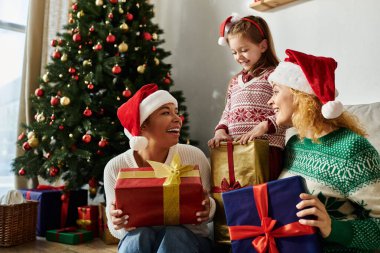 Mutlu bir lezbiyen çift ve kızları Noel ağacının yanında birlikte hediyeleri açmaktan zevk alırlar.