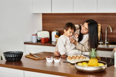 Neşeli bir anne oğlunu modern mutfakta yemek pişirirken, bayram ruhunu kutluyor..