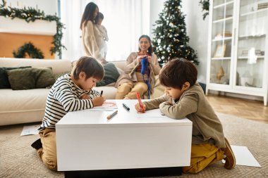 Bir Asyalı aile Noel ağacının etrafında toplanıyor. Çocuklar renkli ve yetişkinler şenlik ruhuna bürünüyor..