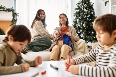 Güzel dekore edilmiş bir Noel ağacının etrafına örgü örüp boyayarak neşeli bir aile birbirine bağlanır..
