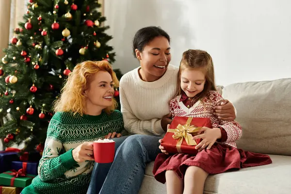 Sevgi dolu bir çift ve kızları, Noel ağacının hediyelerini açarken gülümsüyorlar..