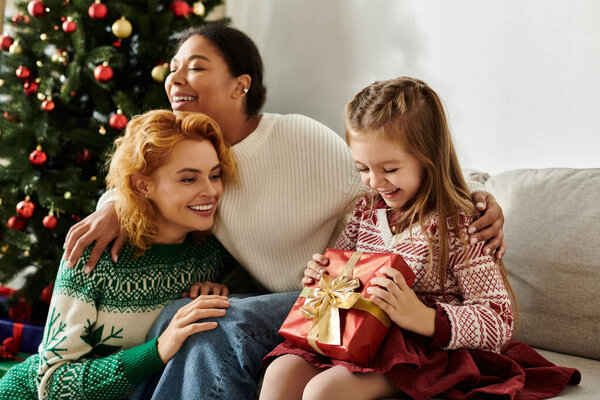 Любящая пара наслаждается праздничным моментом, в то время как их дочь открывает красиво обернутый подарок.