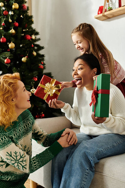 A loving couple shares gifts with their daughter by the festive Christmas tree in their cozy home.
